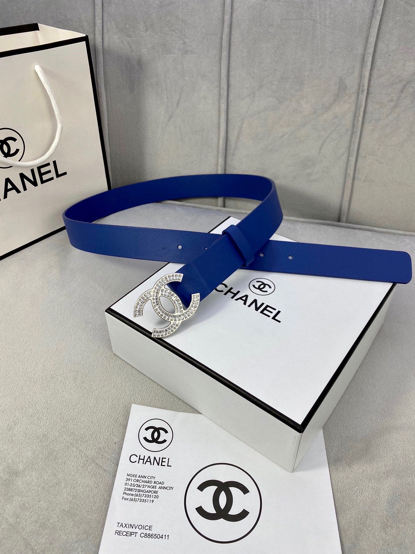 Blue leather belt with rhinestone CC buckle laid across a product box