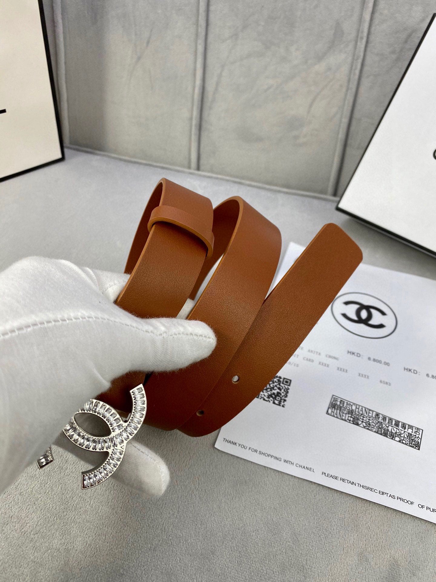Brown leather Chanel belt with rhinestone CC buckle, held over paperwork