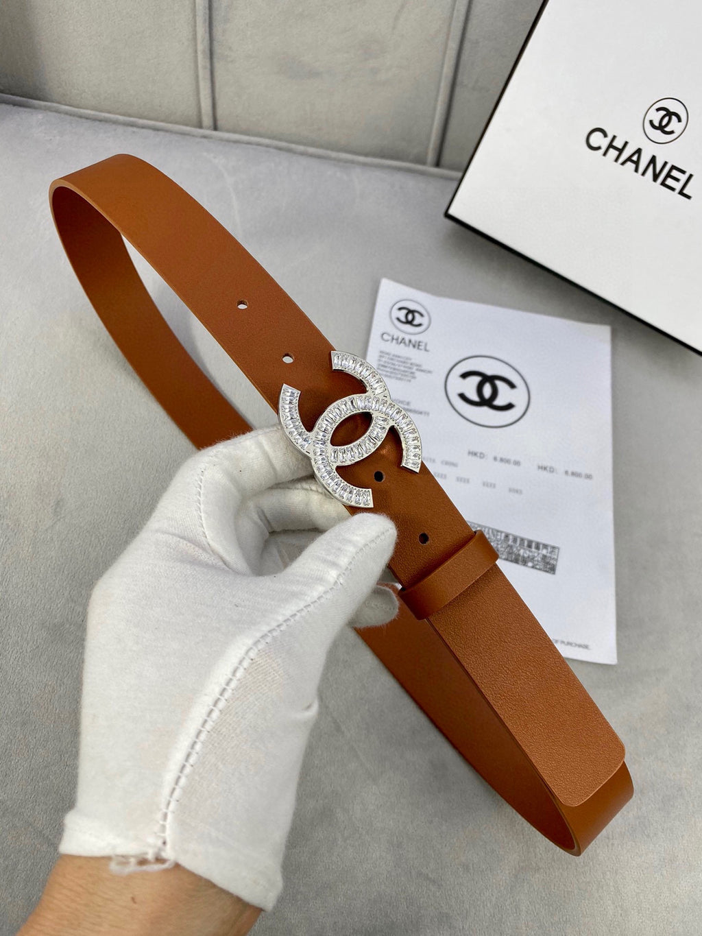 Brown leather Chanel belt with gold-tone rhinestone CC buckle held by a gloved hand