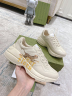 White Gucci unisex sneakers held in hand, tiger graphic on side and lace-up front.