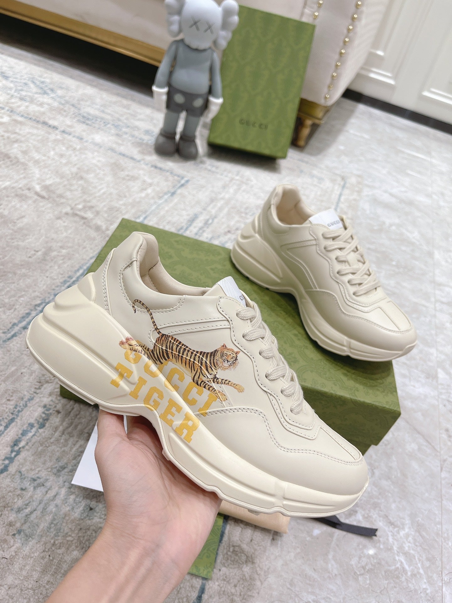 White Gucci unisex sneakers held in hand, tiger graphic on side and lace-up front.