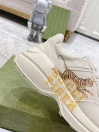 White Gucci unisex sneaker close-up showing tiger graphic and side panel stitching.