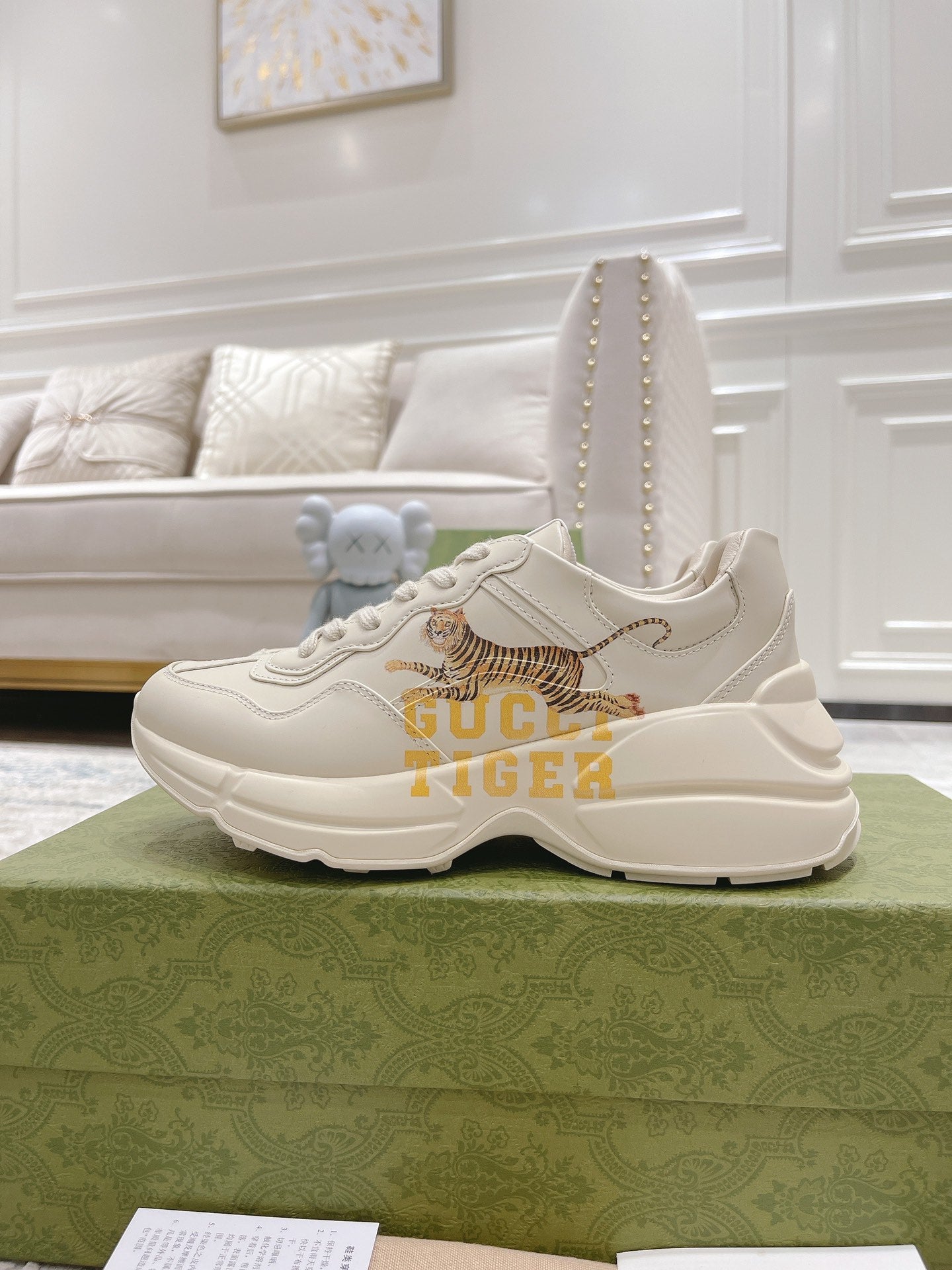 White Gucci unisex sneaker with tiger artwork and thick rubber sole, front view.