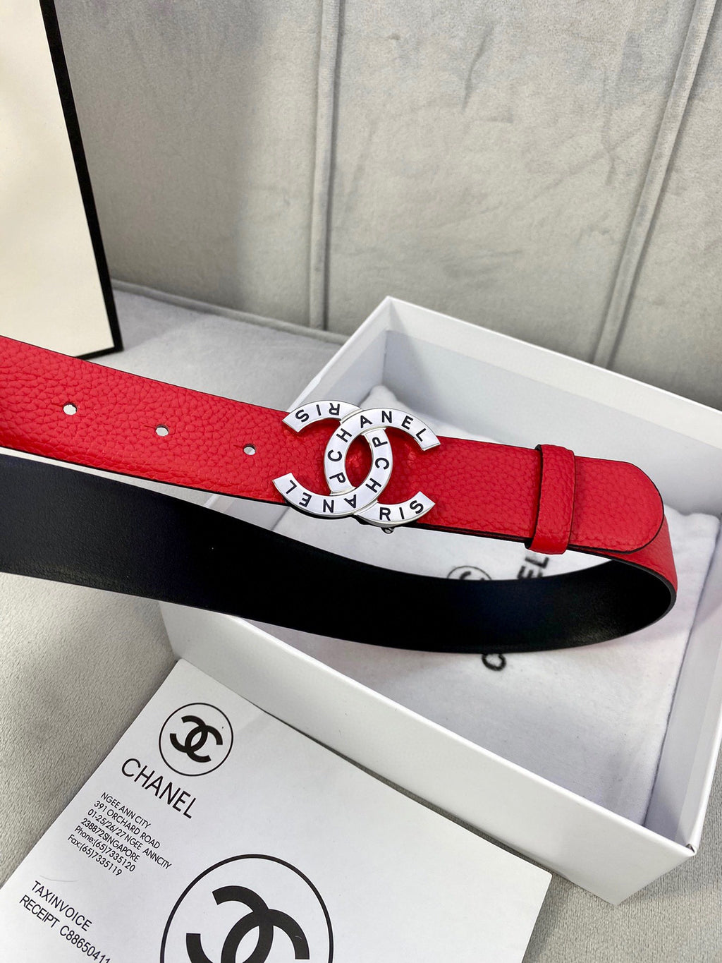 Chanel belt on display box, red strap with gold circular CHANEL buckle and matching hole rows.