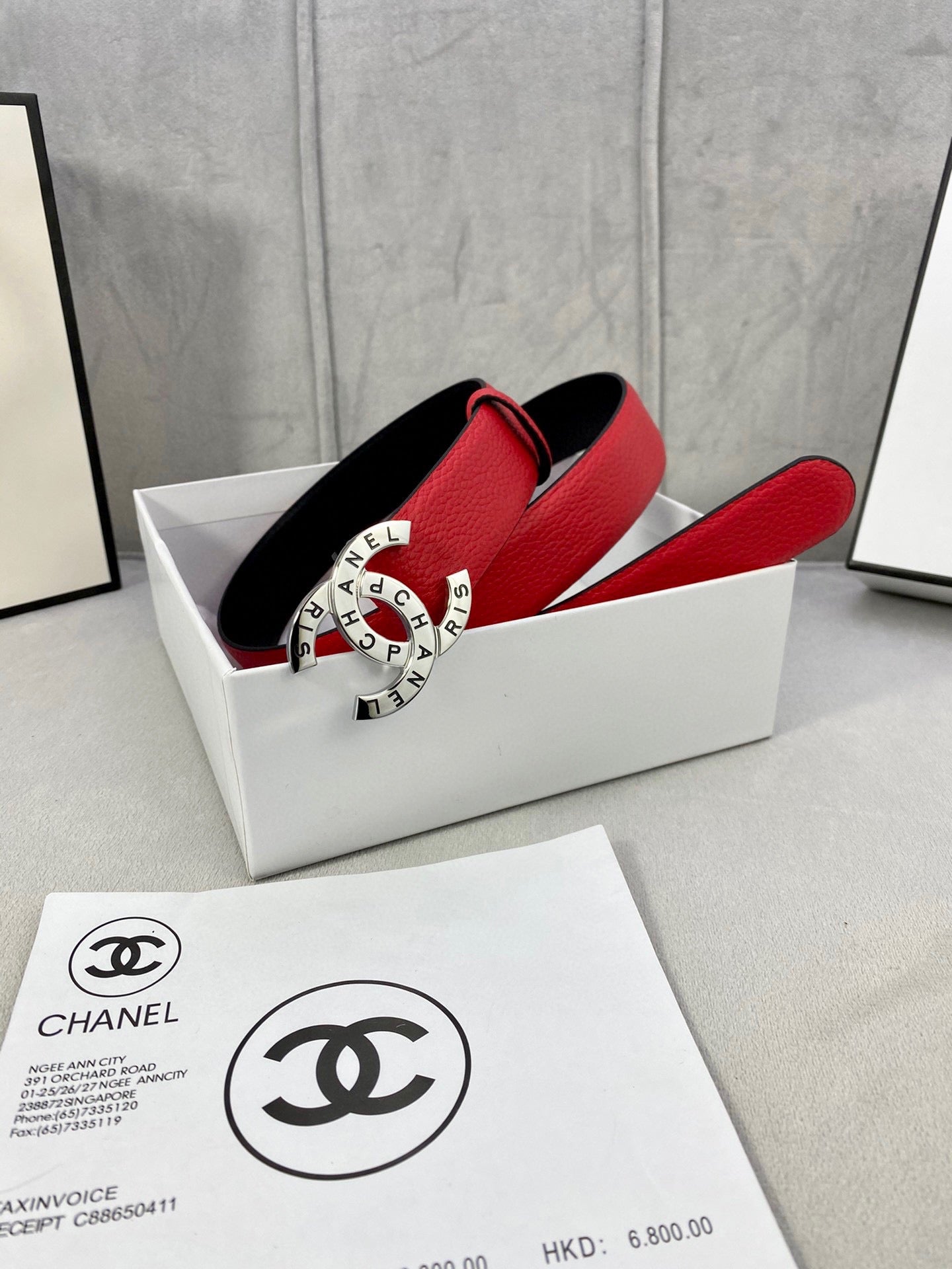 Chanel belt shown in box: red leather strap with holes and gold CHANEL logo buckle.