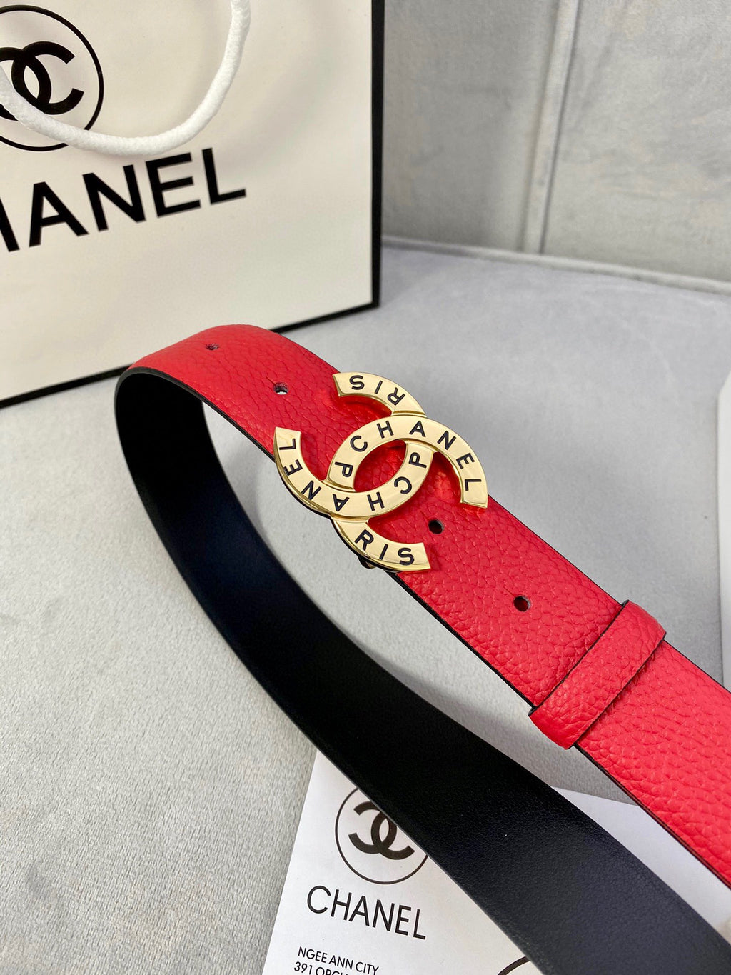Chanel belt side view: red leather strap with gold CHANEL buckle over black inner lining.