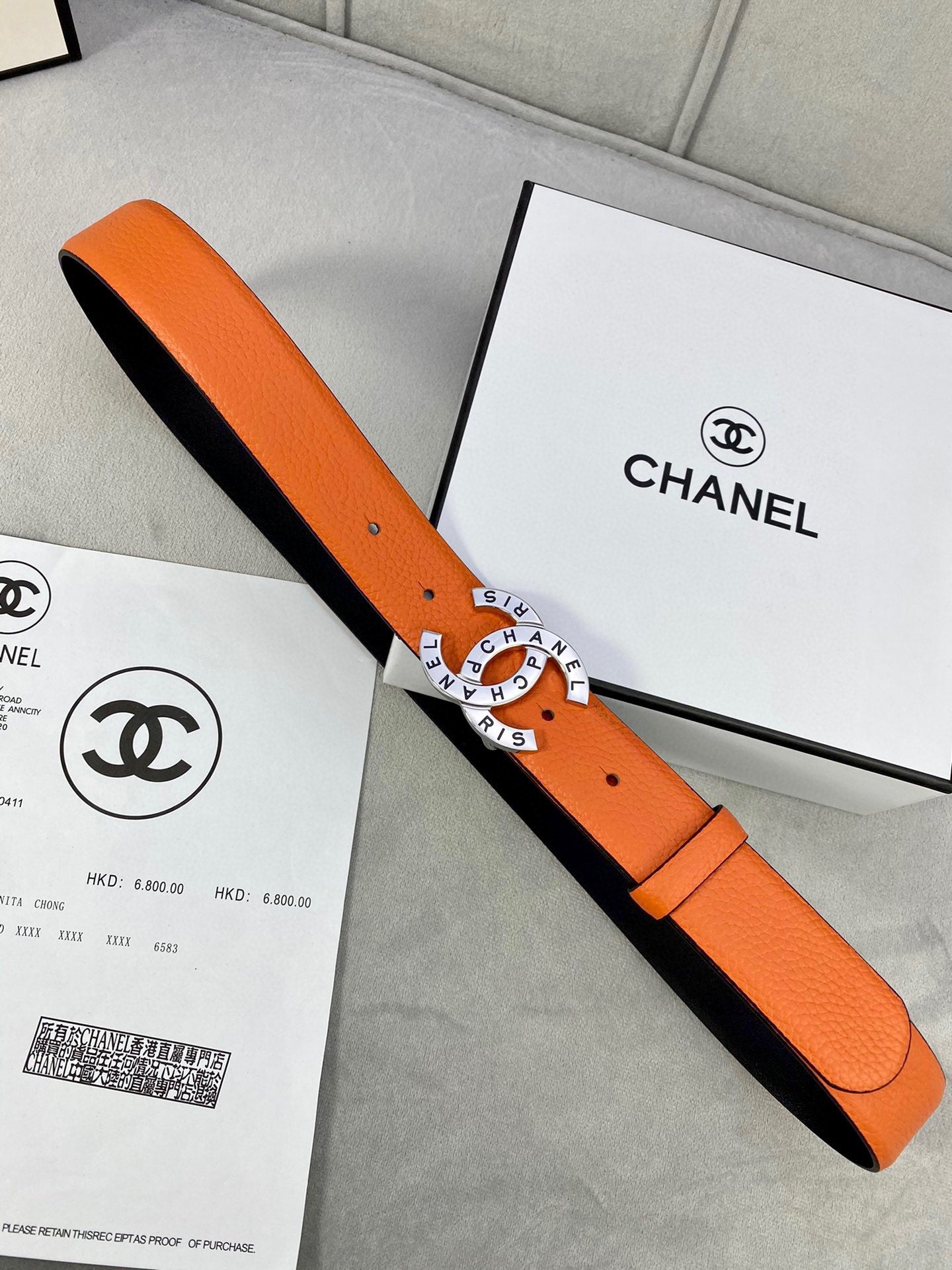 Orange Chanel belt laid across box, black lining and round logo buckle visible