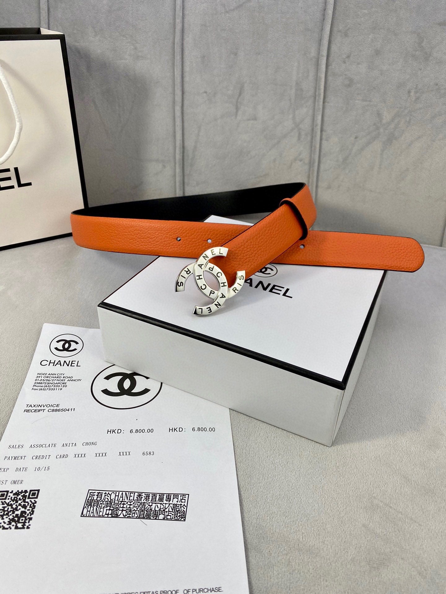 Orange leather belt with black lining and Chanel round logo buckle on packaging