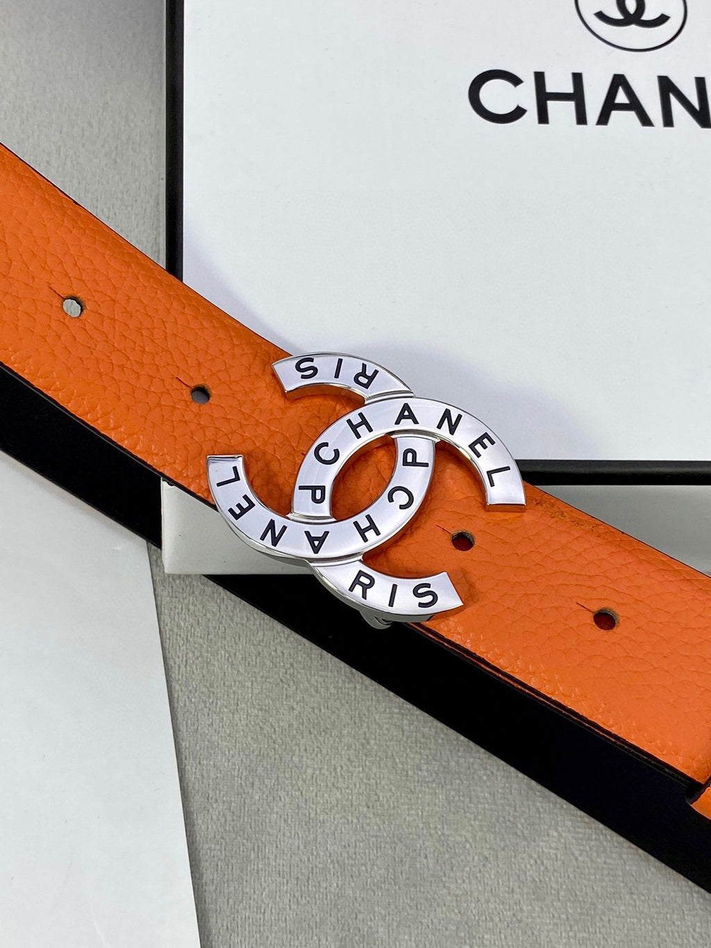 Close-up of orange Chanel belt with black lining and round logo buckle