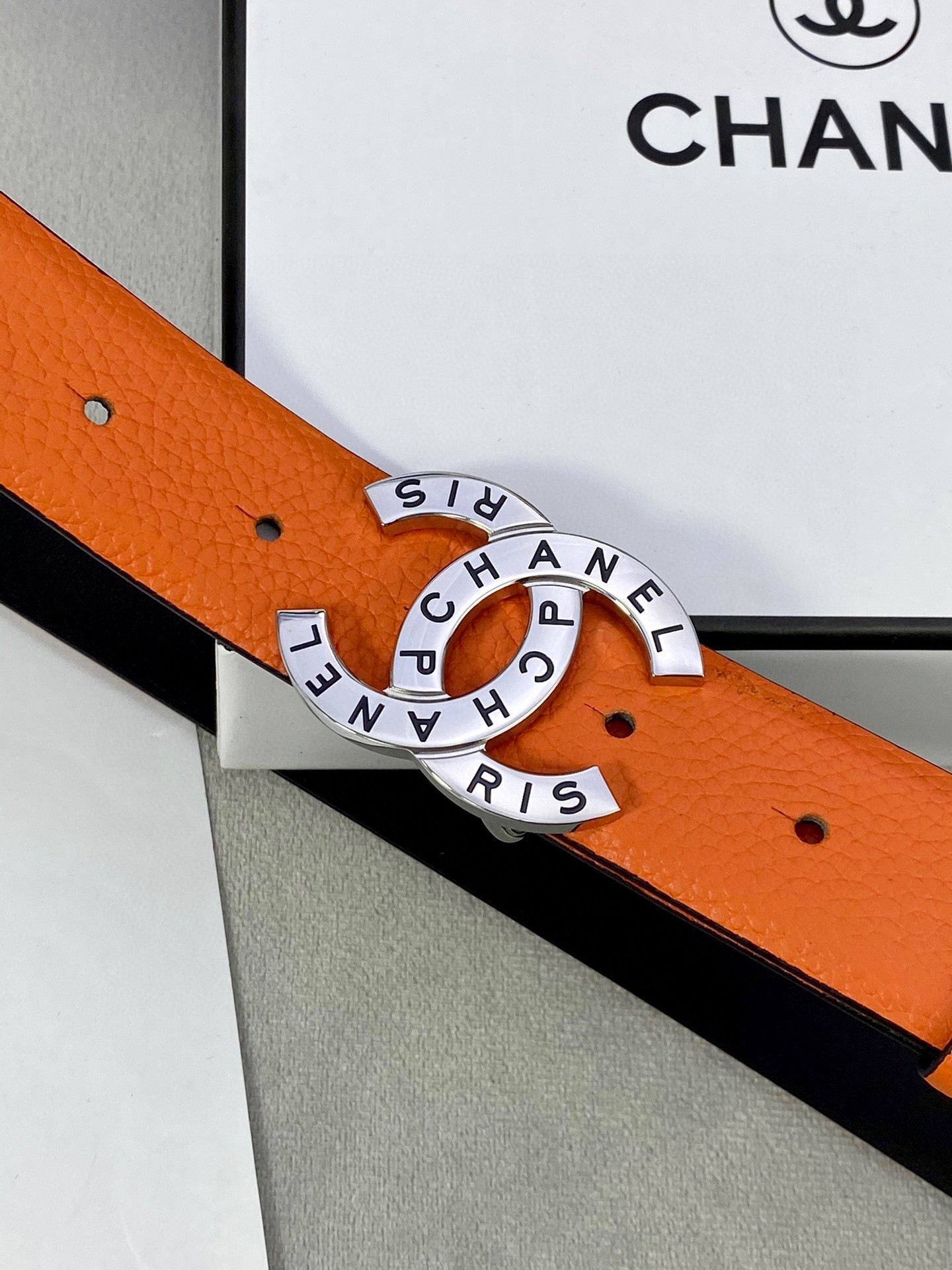 Close-up of orange Chanel belt with black lining and round logo buckle