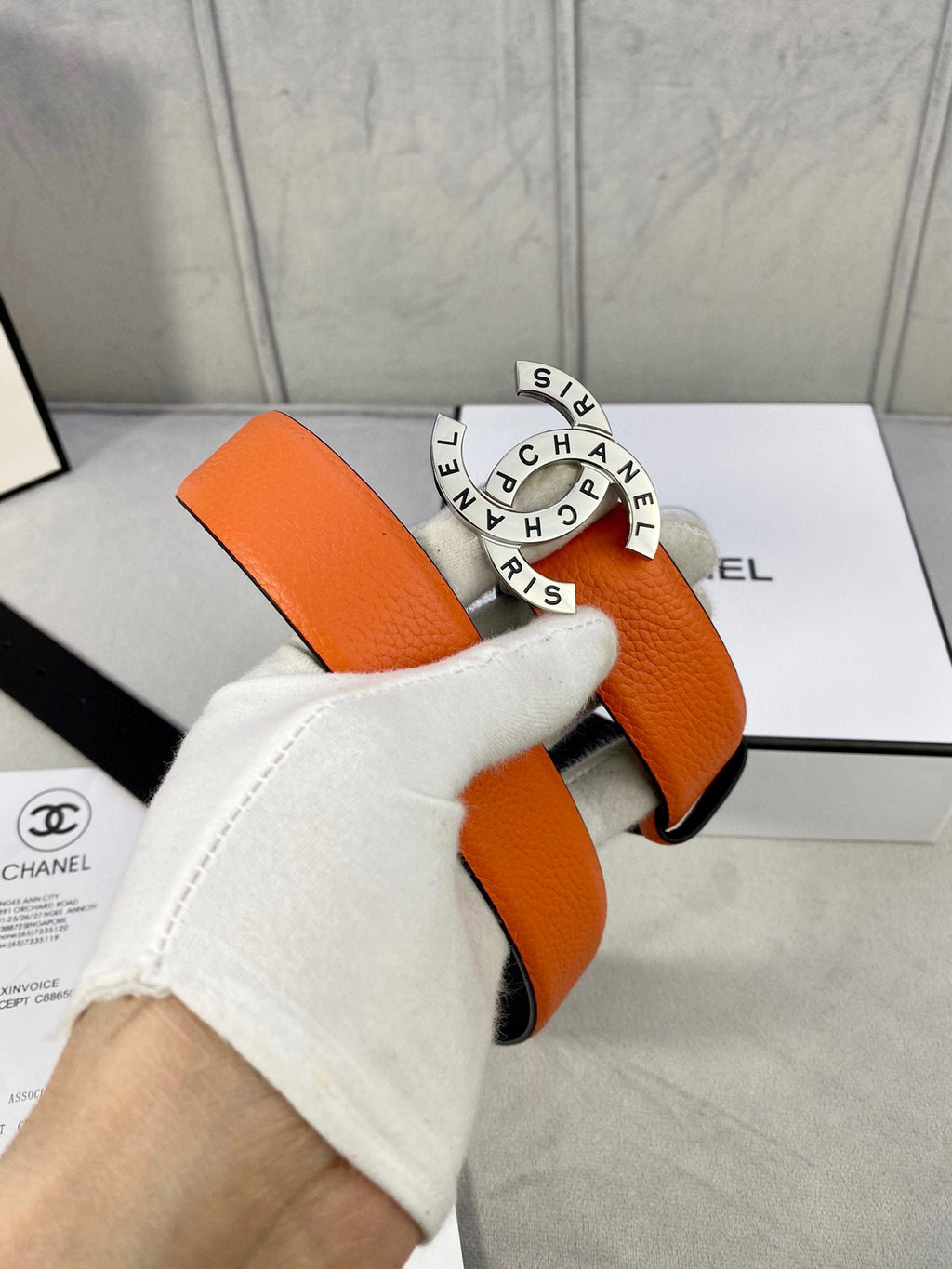 Orange Chanel belt with black underside and round logo buckle held in hand