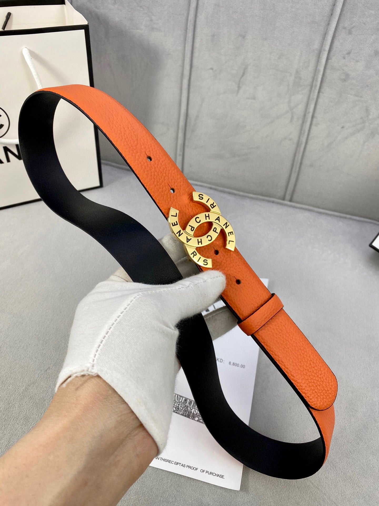 Orange belt with black underside, round Chanel logo buckle on a box