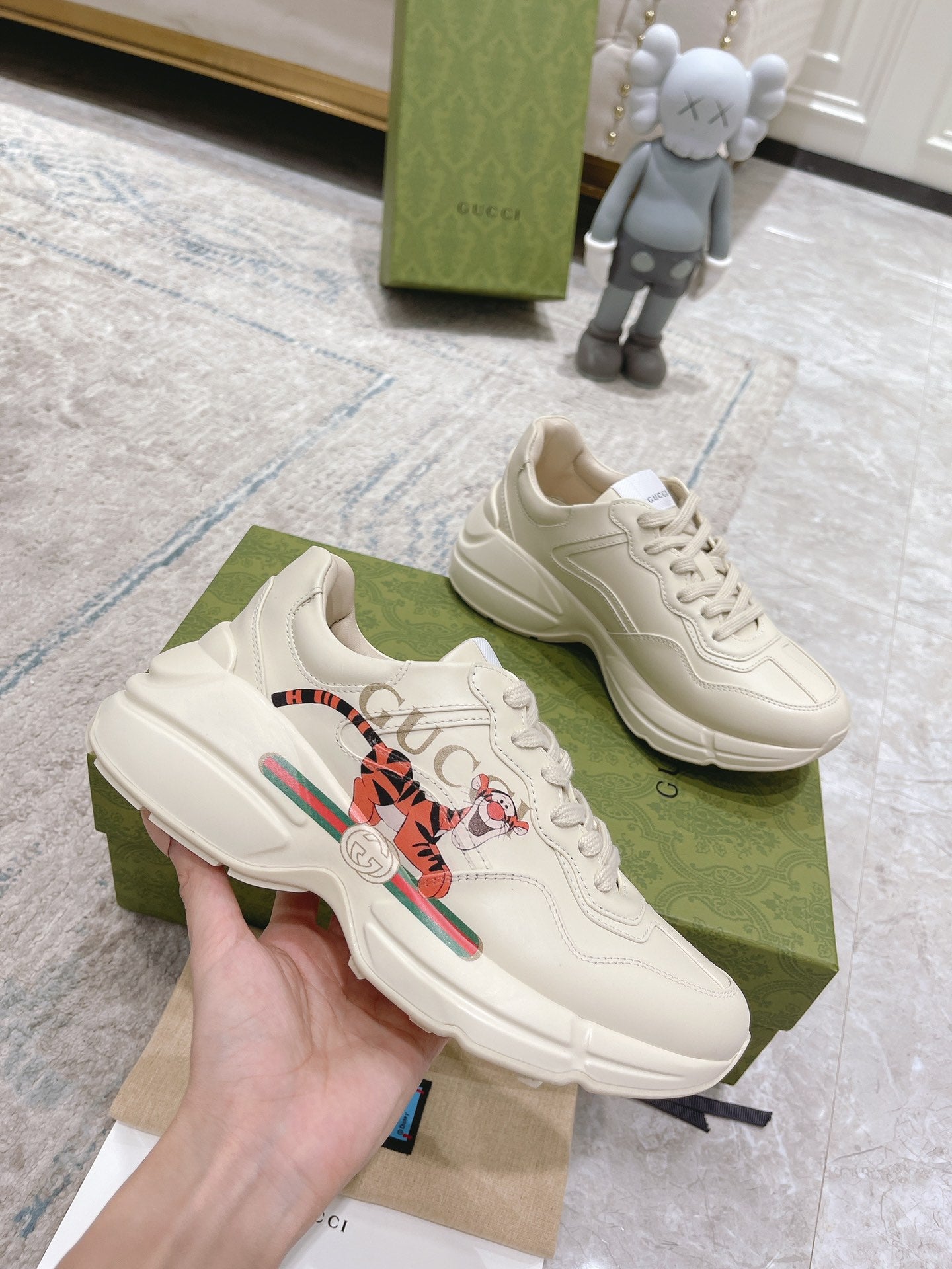 Gucci unisex white luxury sneakers, hand holding one shoe, lace-up and stripe graphic
