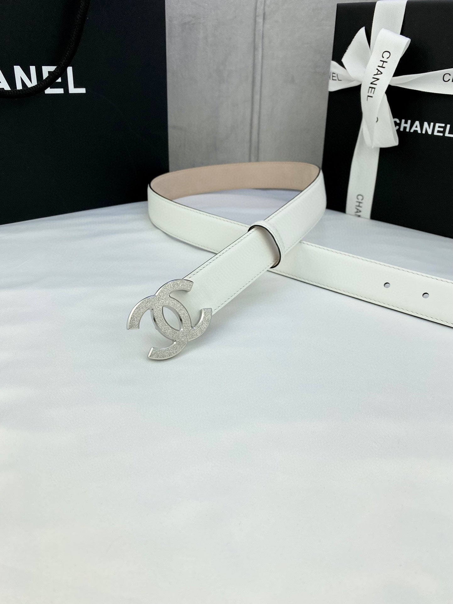 Chanel belt with white leather strap and silver CC buckle accent, resting on surface