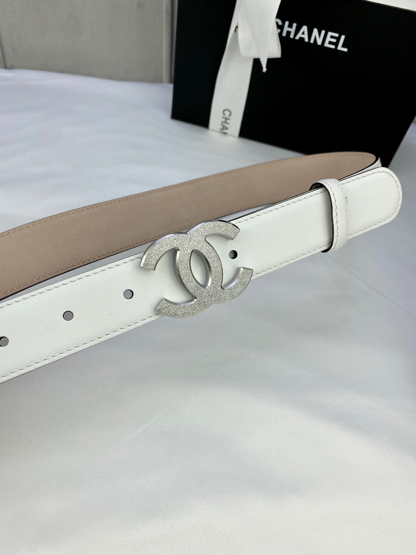 Chanel belt close-up: white leather strap with silver CC logo buckle and eyelet holes
