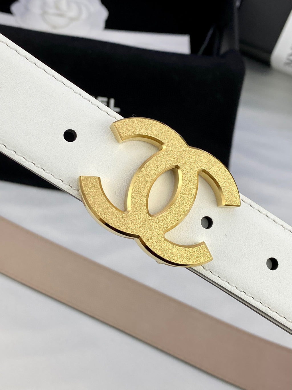 Chanel belt close-up: gold CC buckle on white leather strap with rivet holes