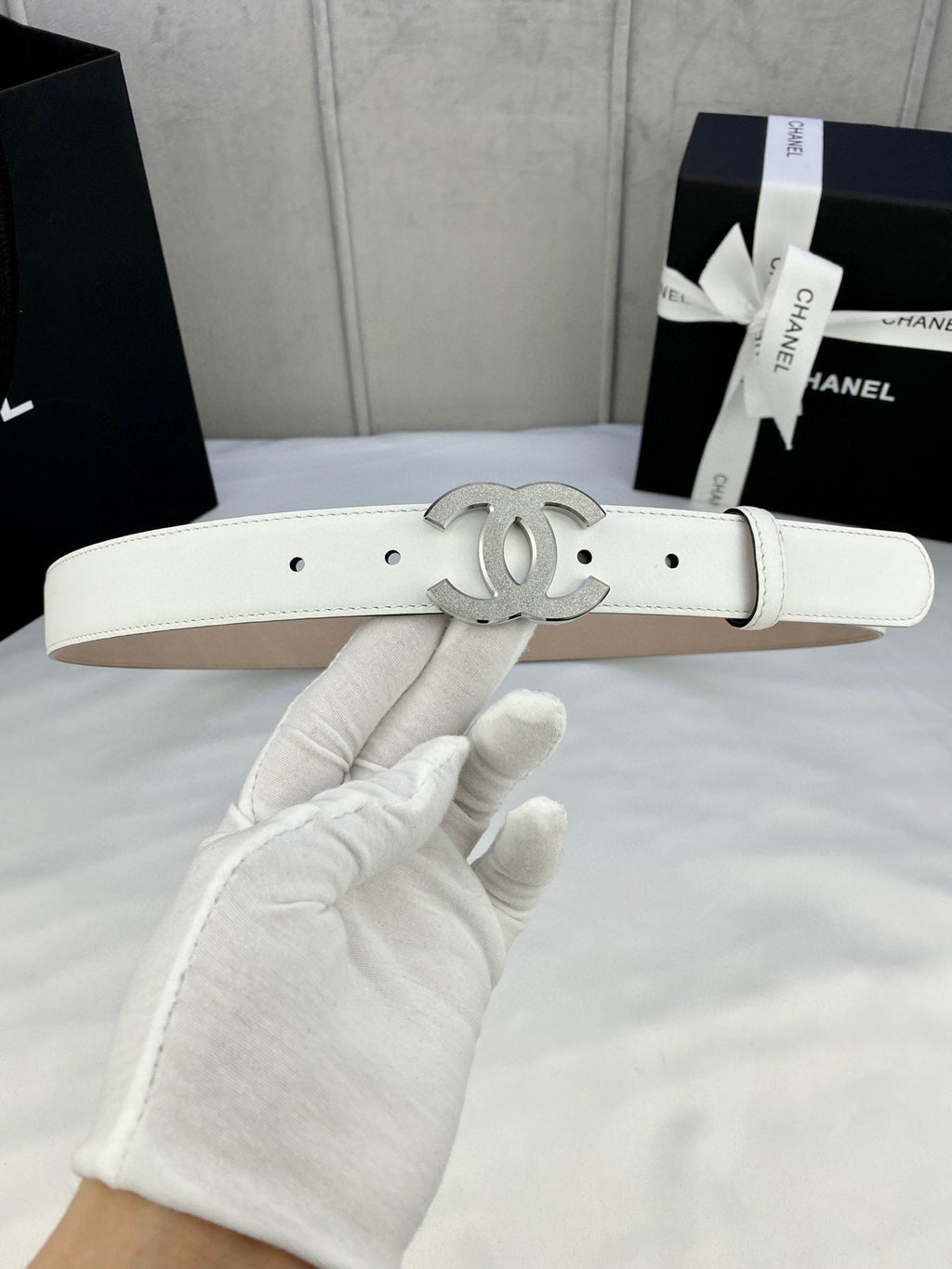 Chanel belt with white leather strap and silver CC logo buckle detail, laid flat