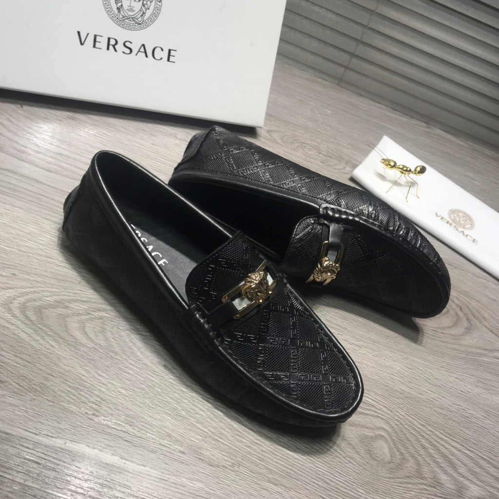 Black Versace loafers with gold buckle and textured logo pattern on the upper.