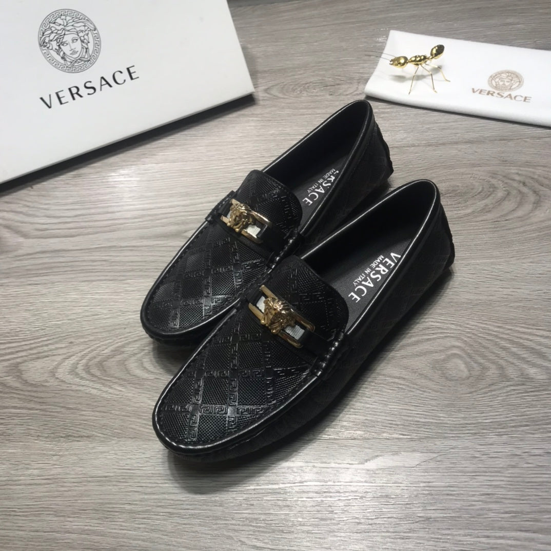 Black Versace loafers with gold buckle hardware over a textured monogram upper.