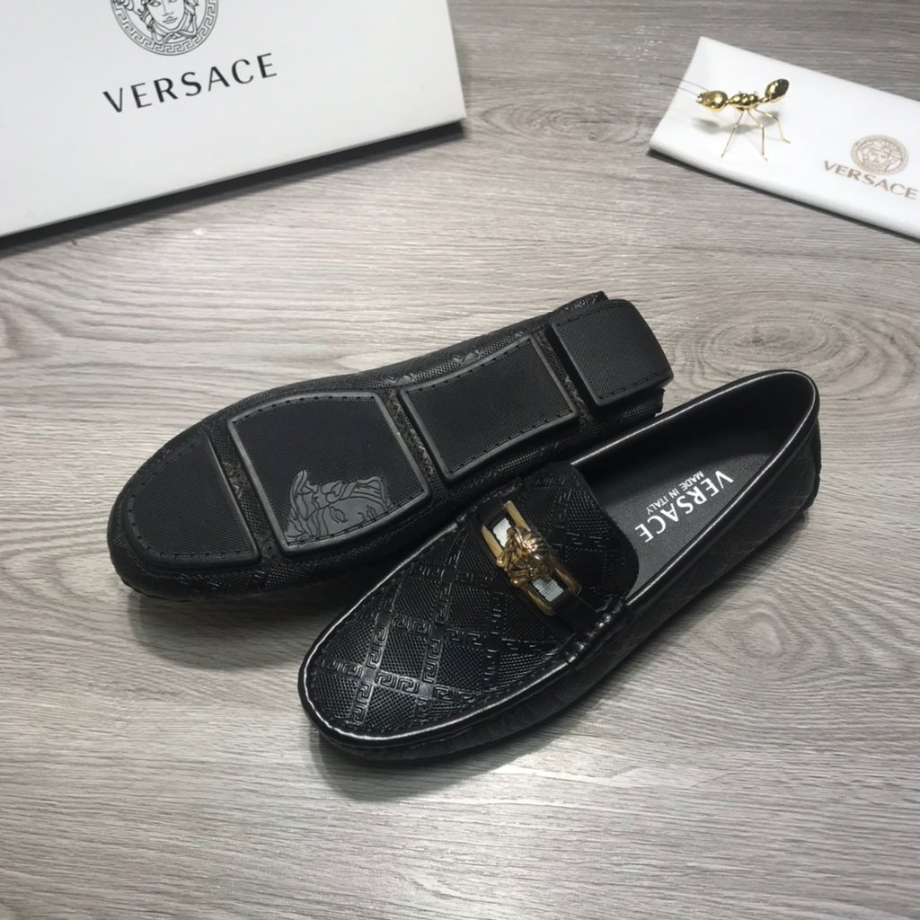 Black Versace loafers with gold buckle on textured pattern across the top.