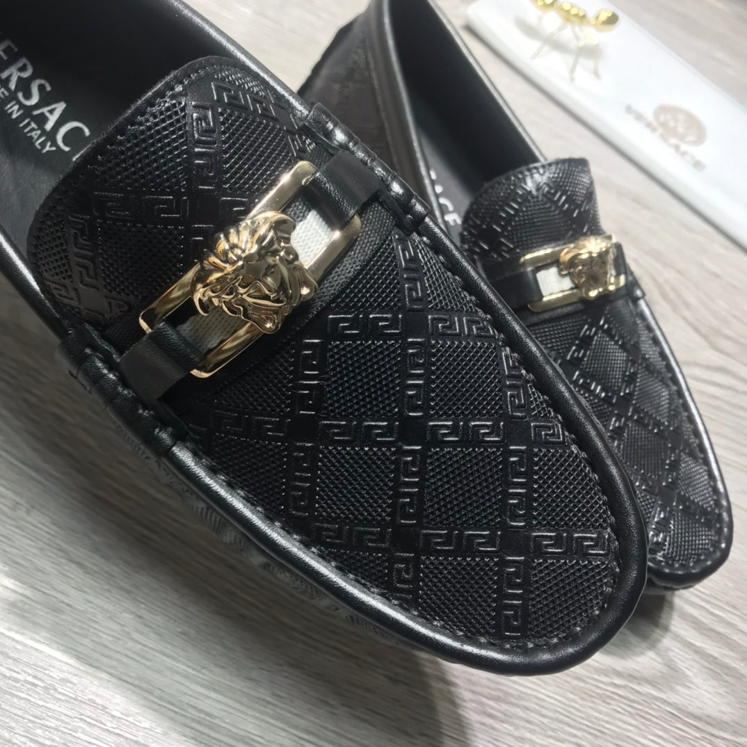 Black Versace loafers close-up showing textured monogram and gold buckle detail.