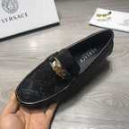 Black Versace loafer held in hand, textured logo upper with gold buckle.