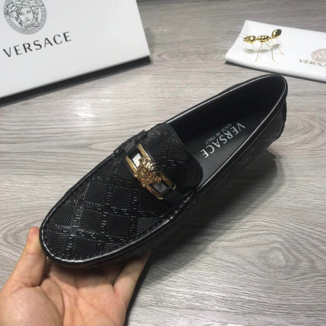 Black Versace loafer held in hand, textured logo upper with gold buckle.