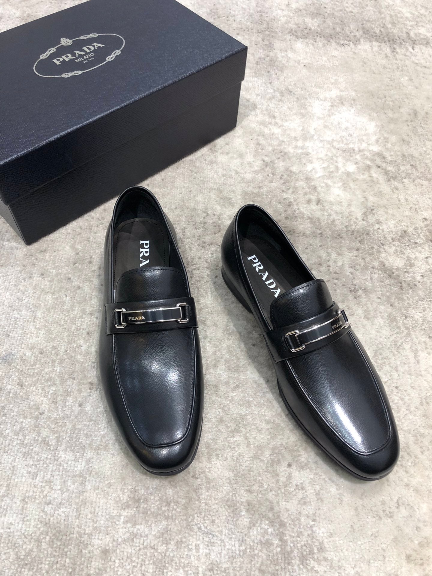 Prada unisex loafers, black leather slip-on with buckle strap, angled view