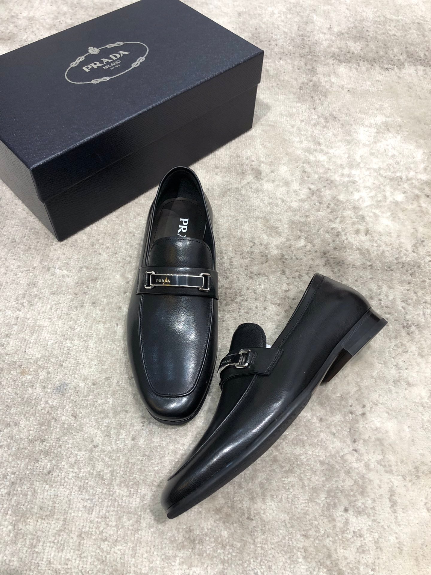 Prada unisex loafers, black leather slip-on pair with buckle strap, one angled