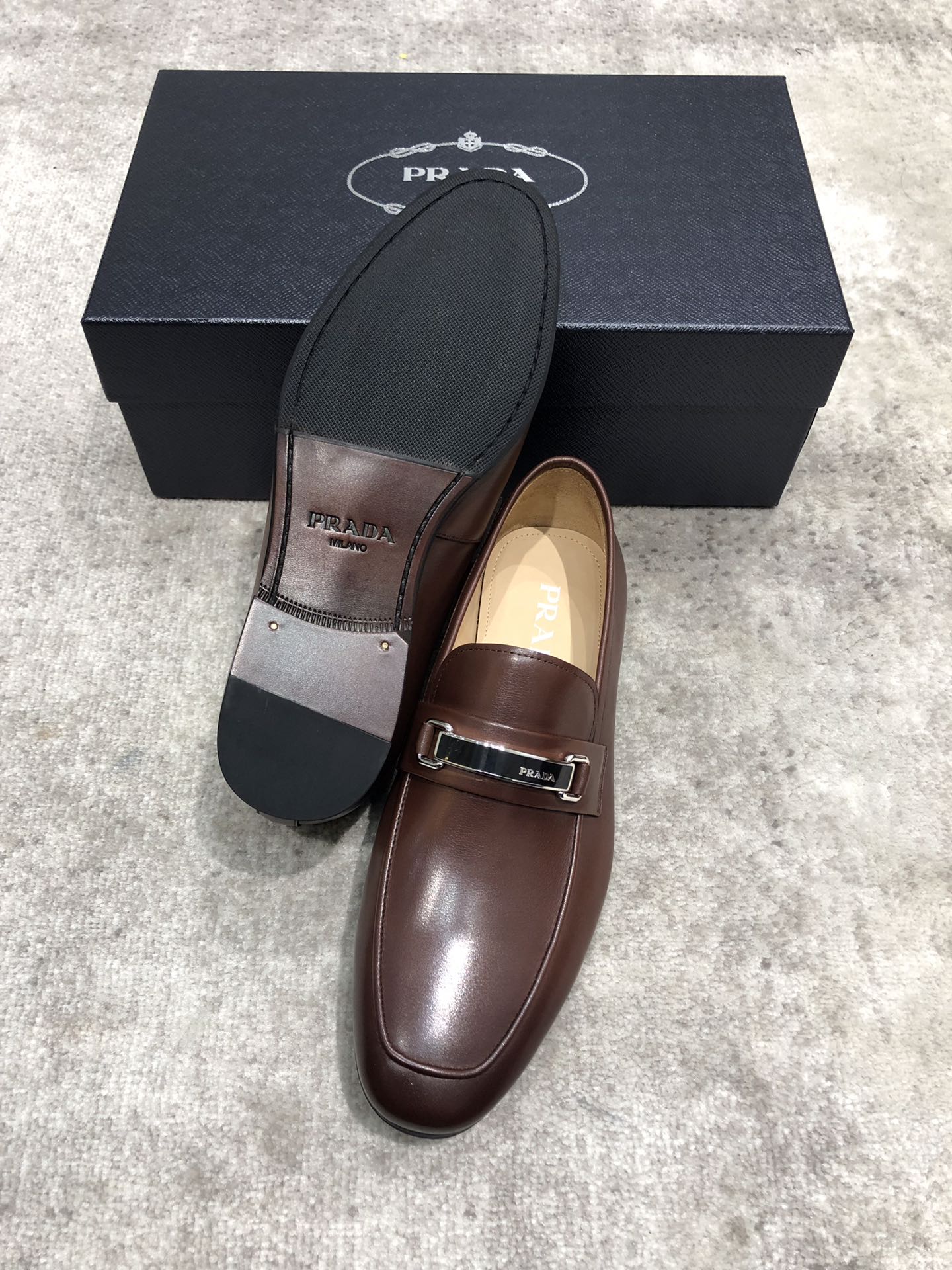 Prada leather loafers, dark brown slip-on with metal buckle strap; visible outsole