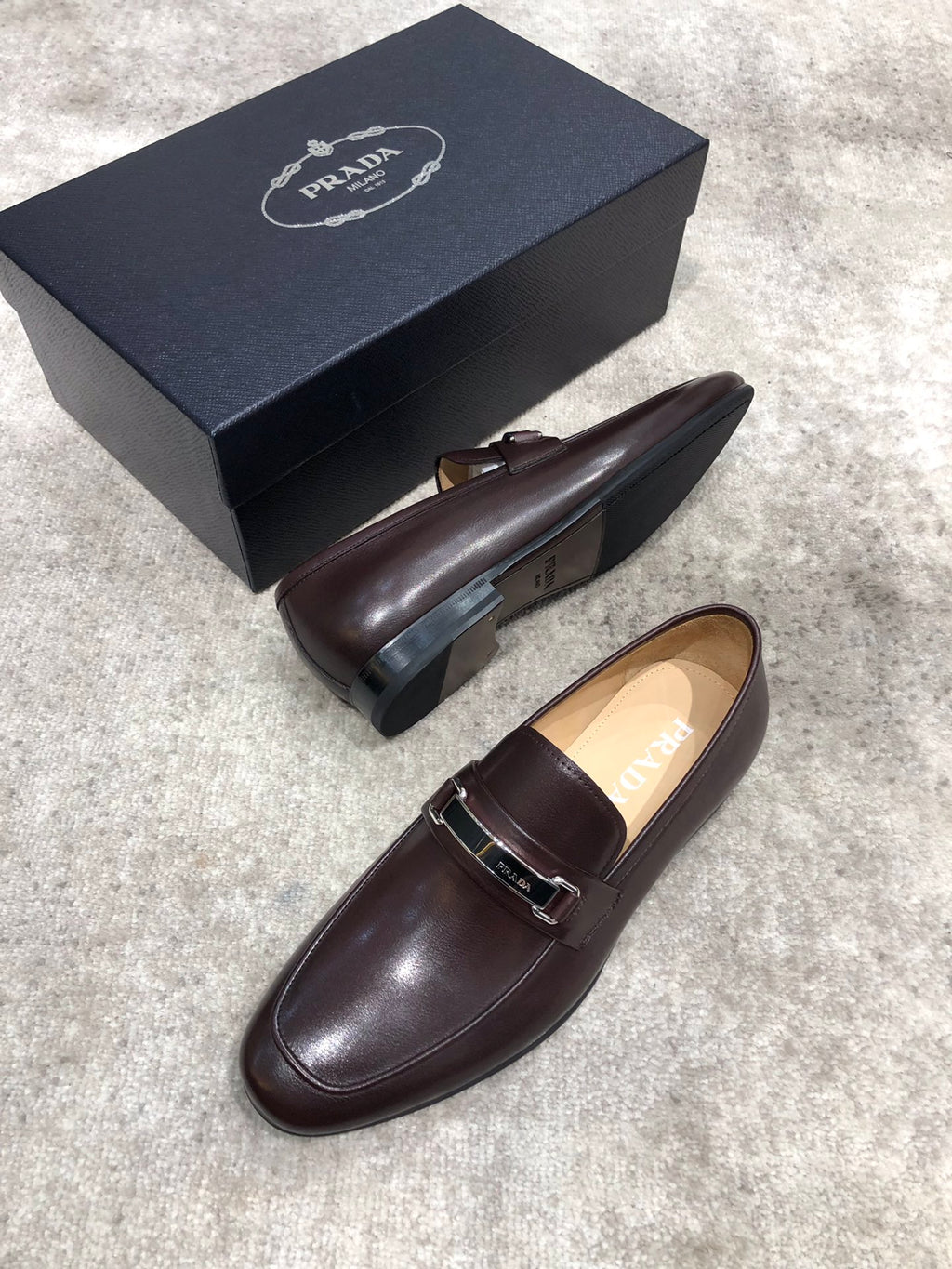 Prada unisex leather loafers, dark brown, front view with metal buckle strap