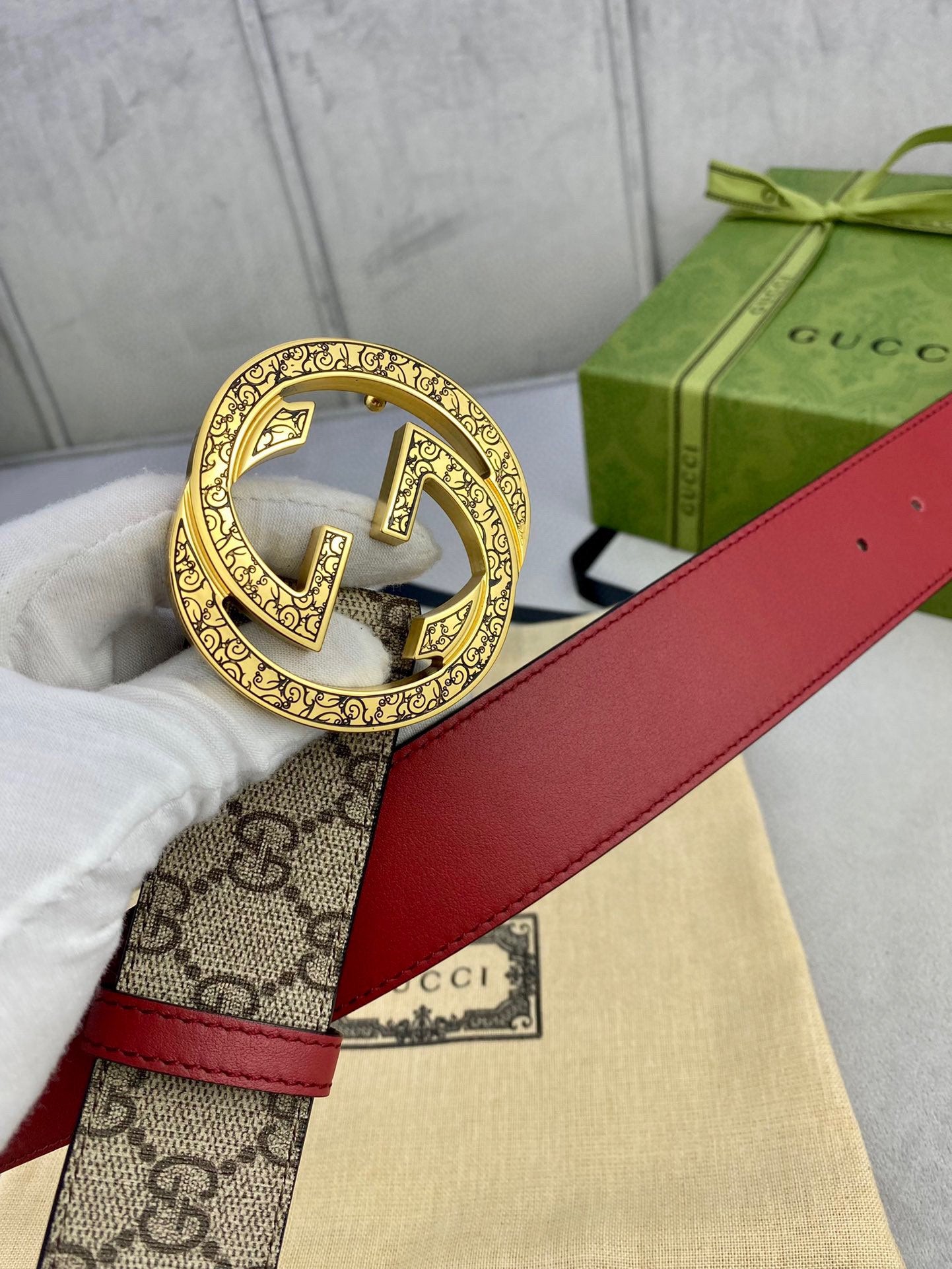 Gucci belt close-up: round gold-tone G buckle on beige GG canvas with red leather strap.