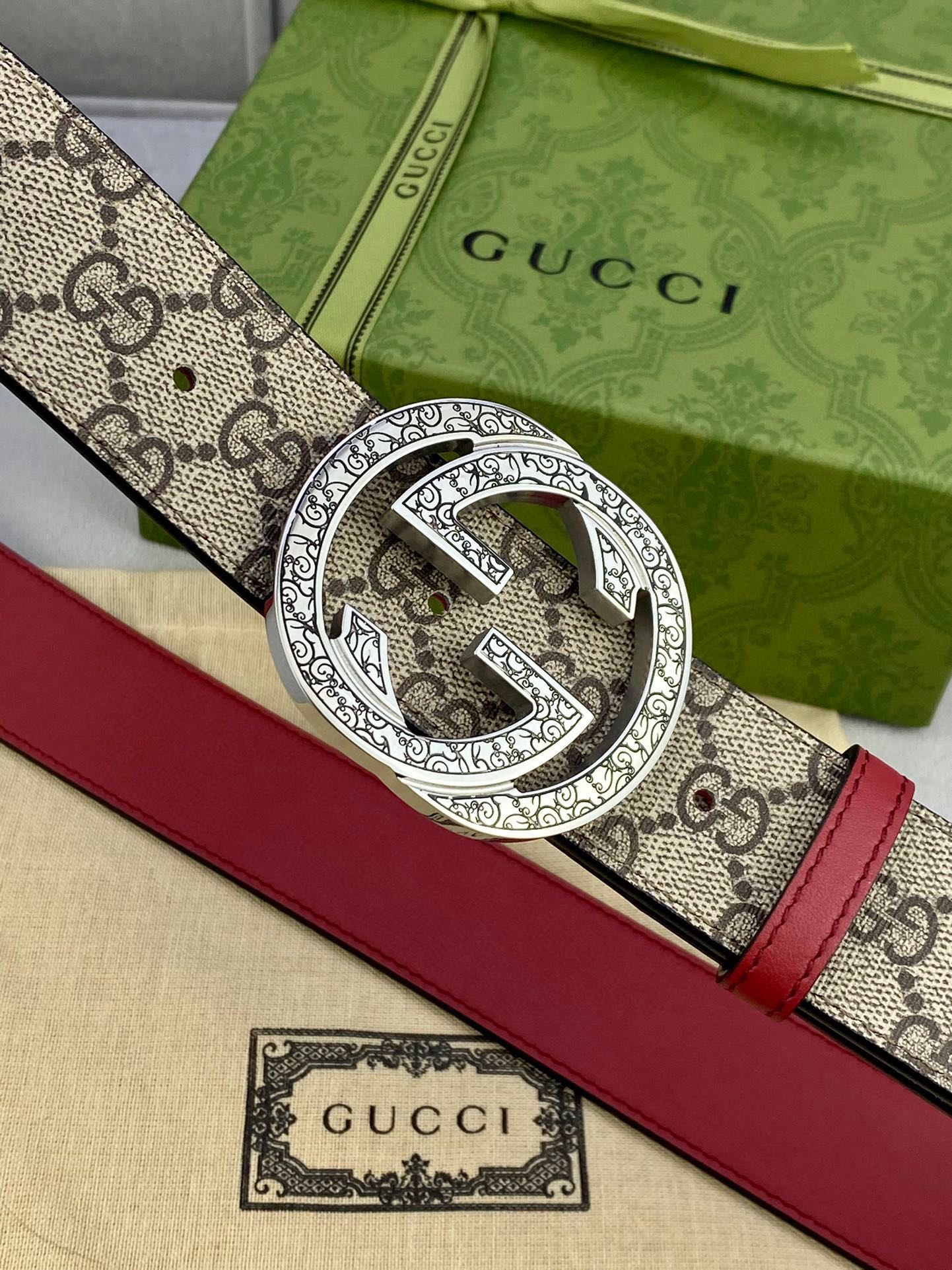Gucci belt buckle close-up: silver-toned G logo on beige GG canvas with red leather edge.