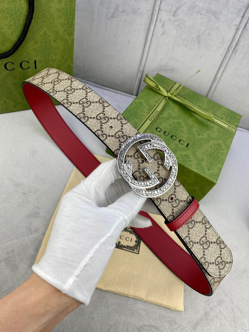 Gucci belt on hand: beige GG canvas strap, red lining, large silver-toned G buckle.