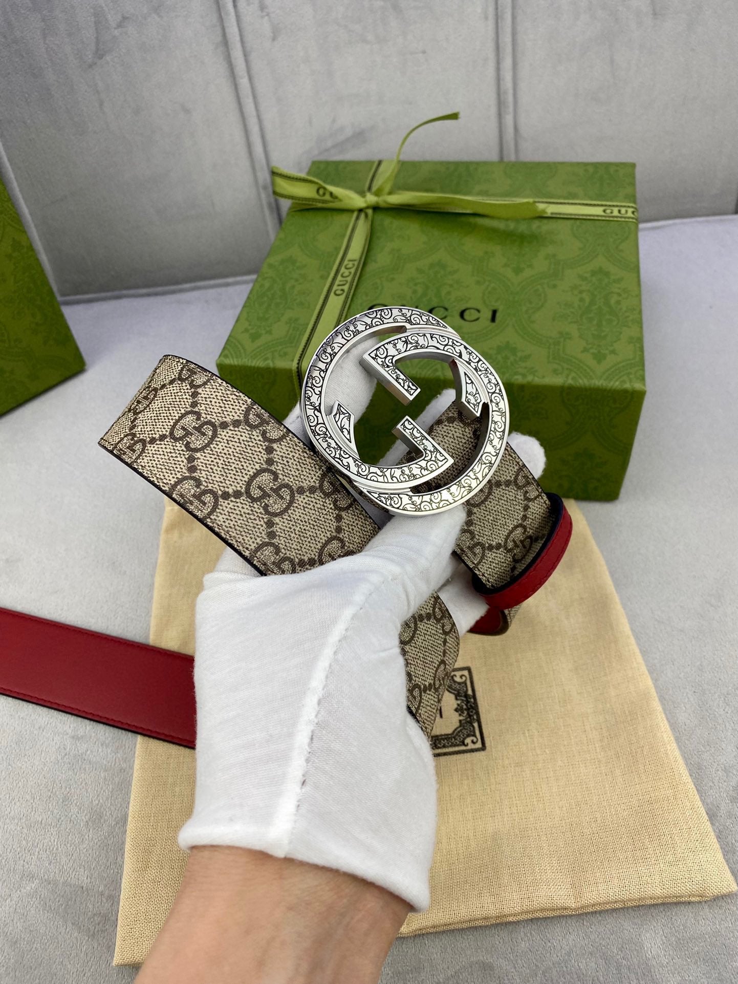 Gucci belt on glove: beige GG canvas strap with red leather and ornate silver-toned G buckle.