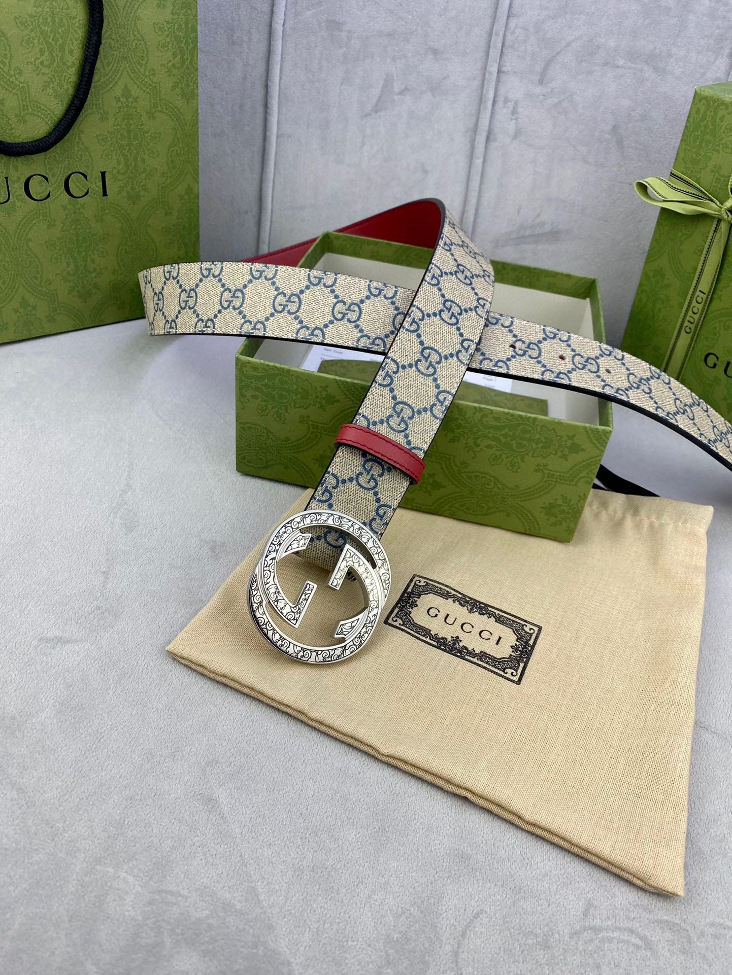 Gucci GG canvas belt with red leather strap and silver-tone G buckle, laid on pouch