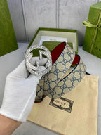 Gucci GG canvas belt with red leather lining and ornate silver-tone G buckle, held up