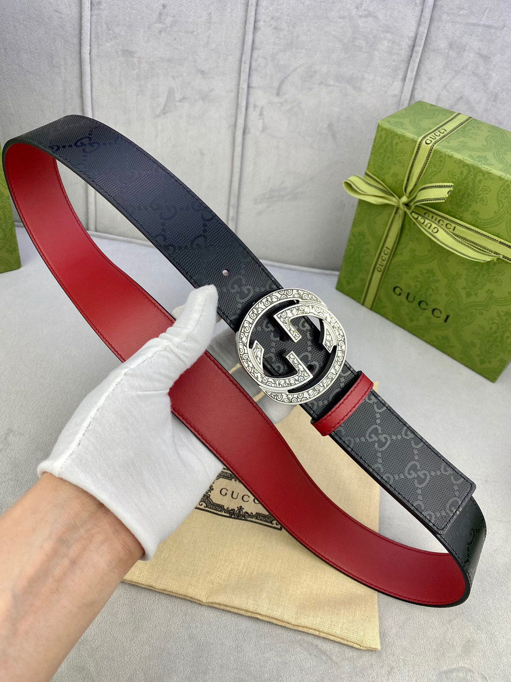 Gucci belt held in hand, dark logo strap with red underside and gold buckle