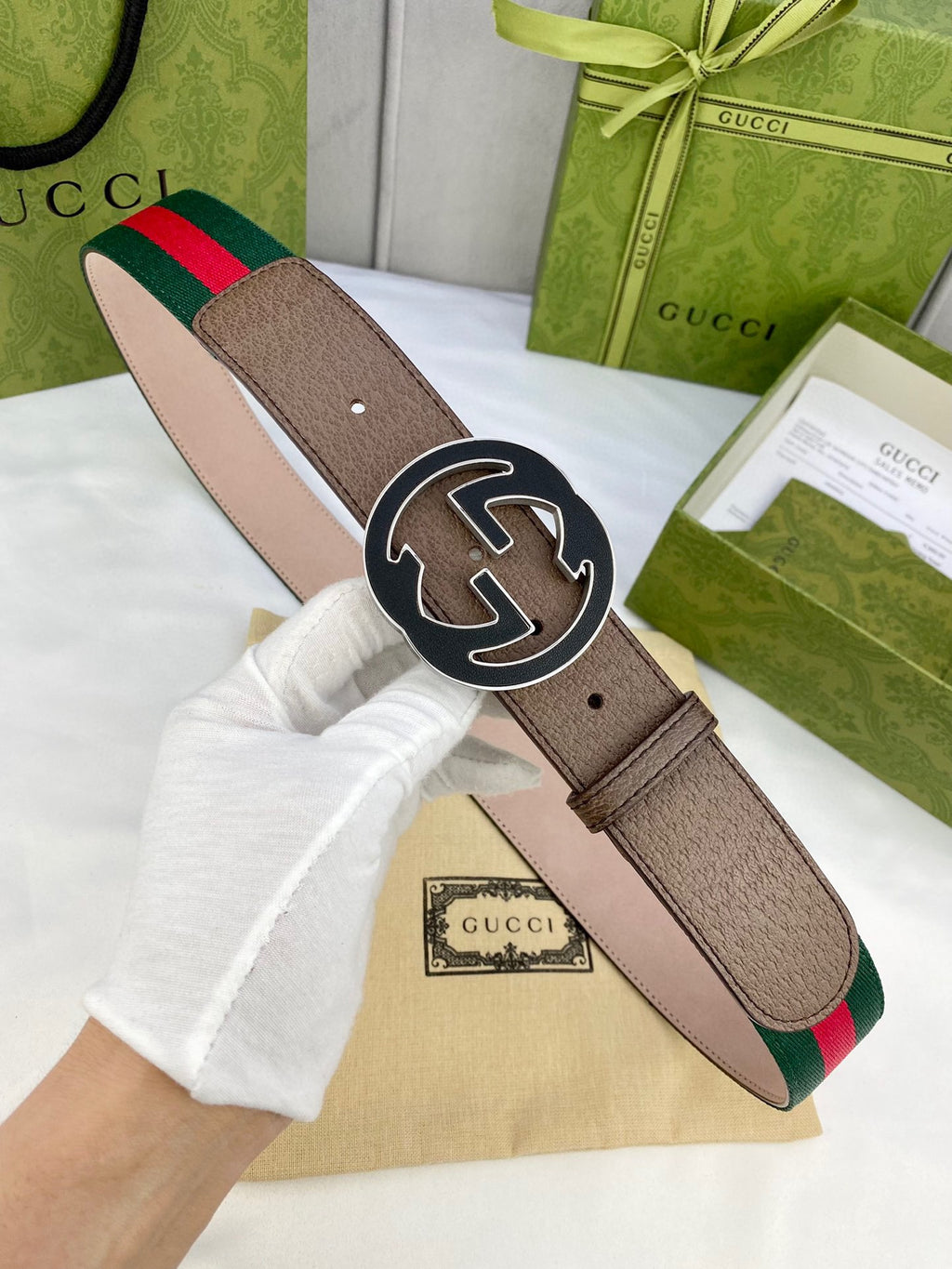Gucci belt worn on a model’s hand: brown leather, green-and-red web stripe, gold-tone buckle.