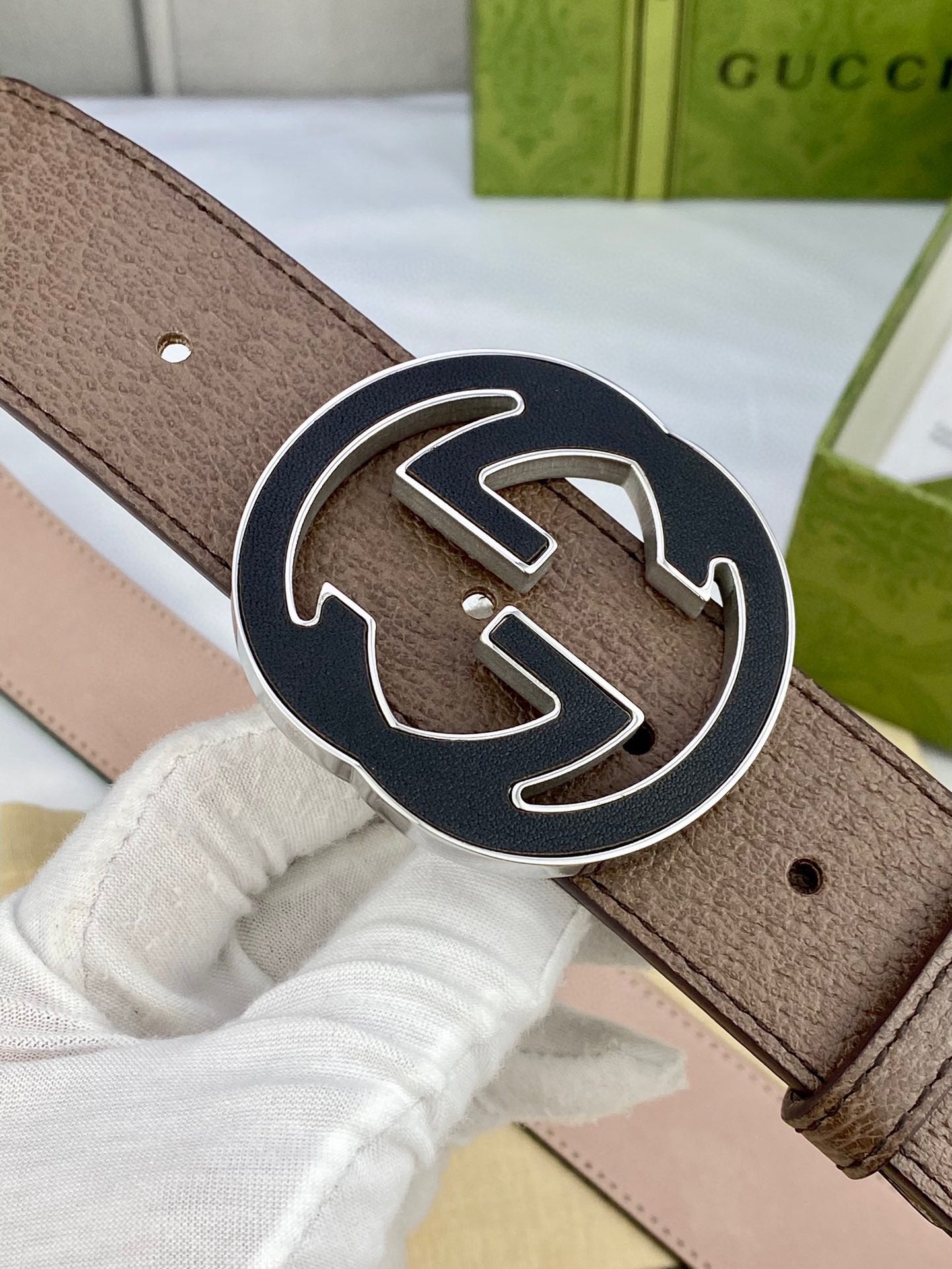 Gucci belt close-up of brown leather and large gold-tone circular GG buckle with dark outline.