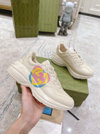 White Gucci unisex sneakers with multicolor GG heart logo, held in hand