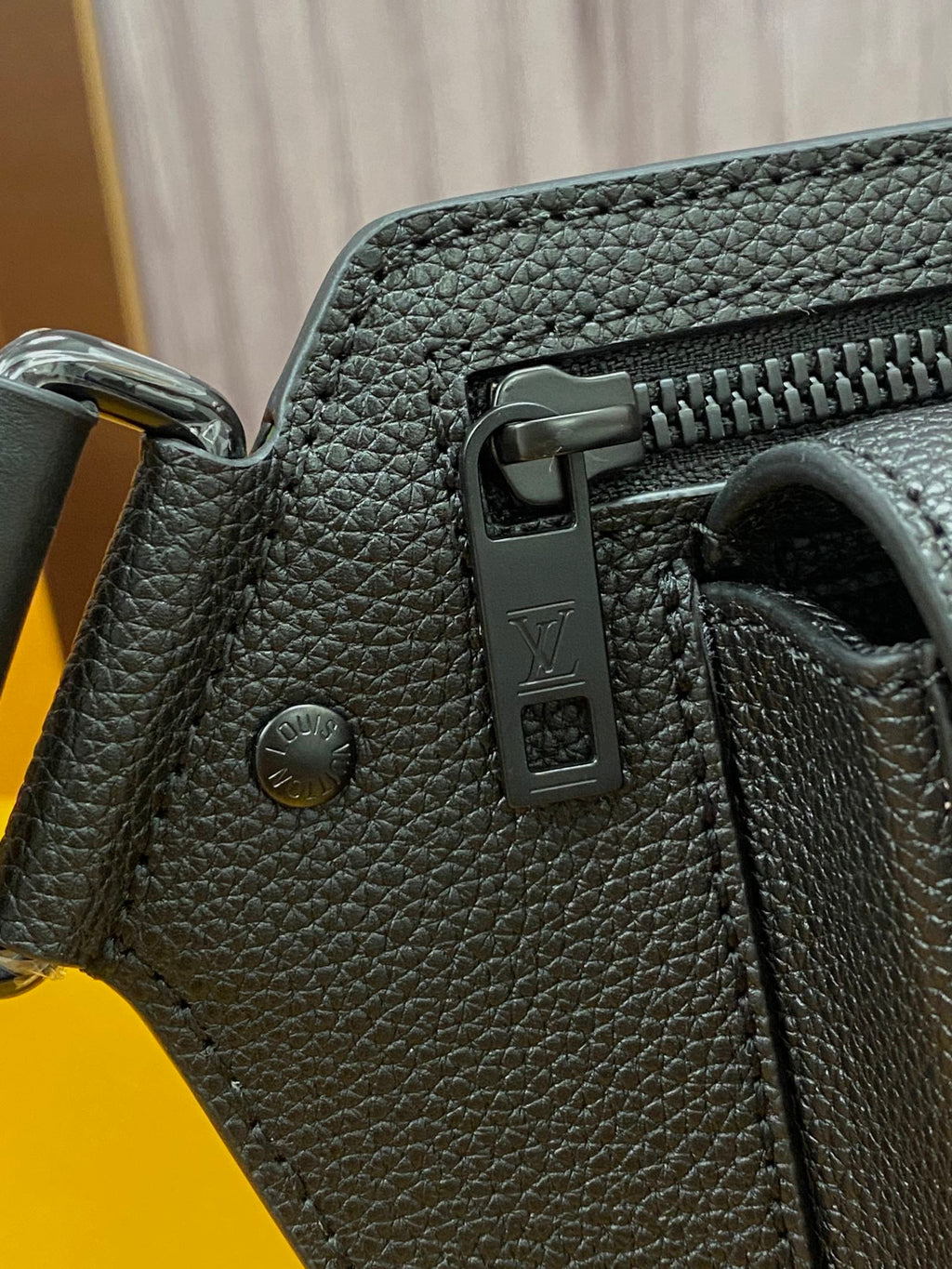 Louis Vuitton bag side view with dark textured leather, snap hardware, and zipper pull