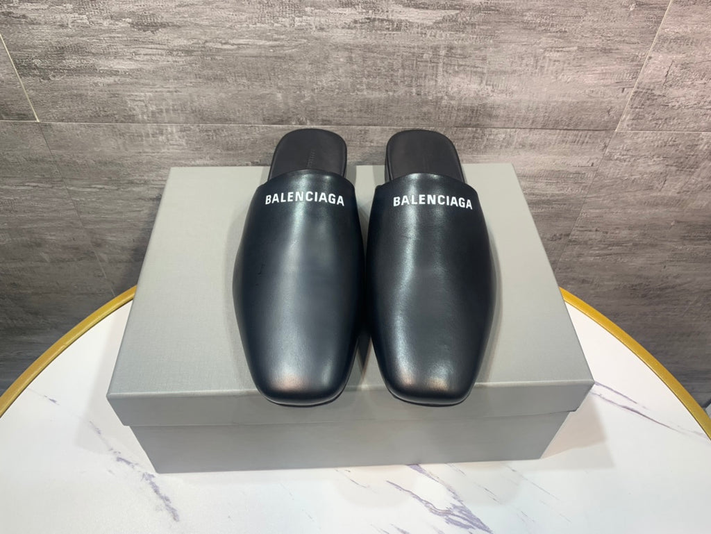 Black leather slide sandals on a box, BALENCIAGA logos on front straps