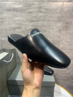 Black leather slide sandals with BALENCIAGA logo strap, held up