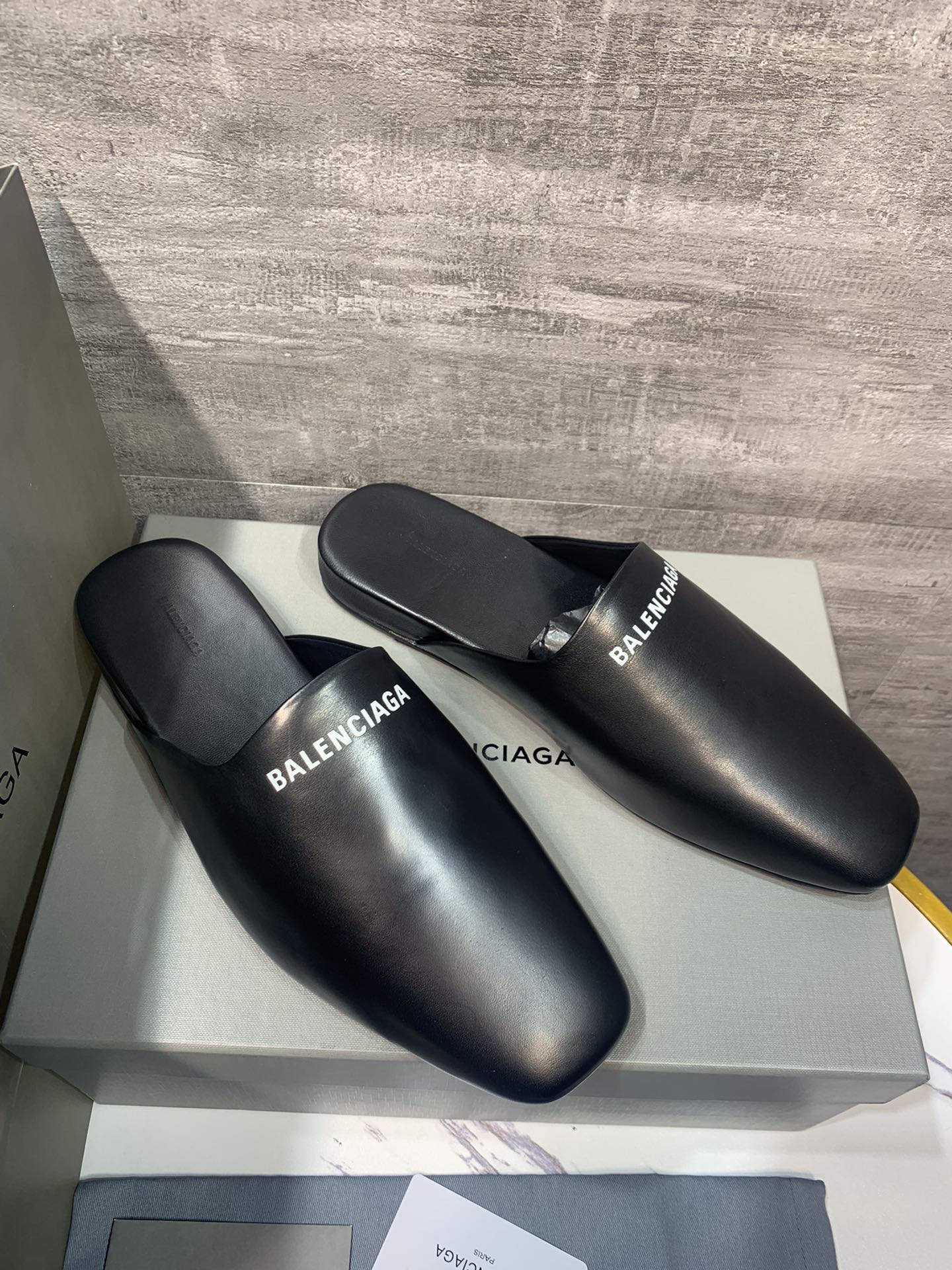 Black leather slide sandals on display box, BALENCIAGA logo on straps