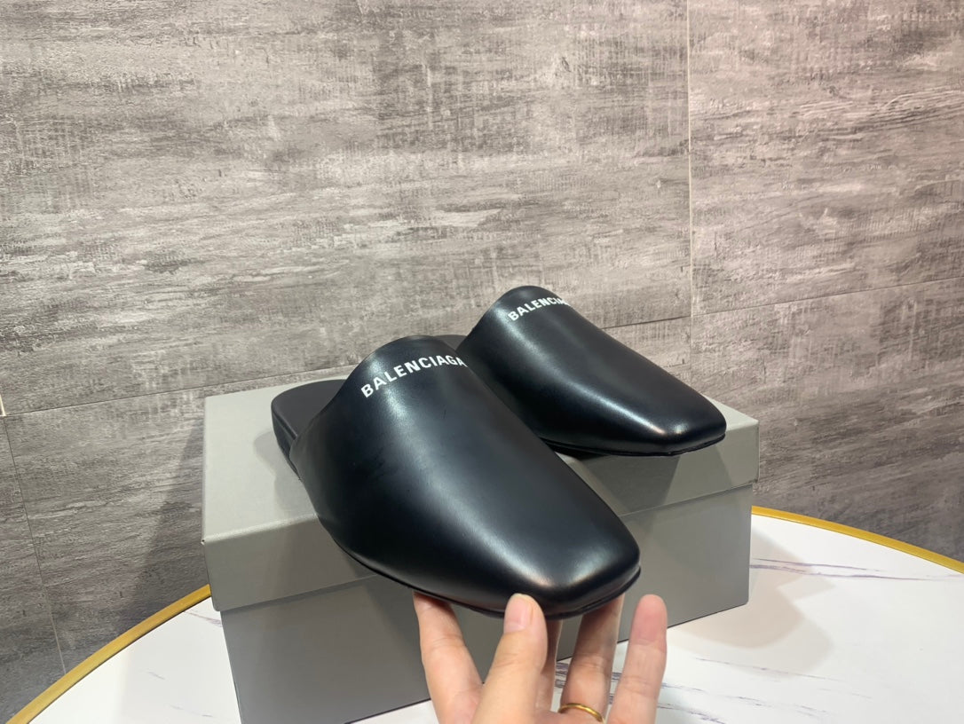 Pair of black leather slide sandals on a box, BALENCIAGA logo straps