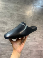 Black leather slide sandal held in hand, BALENCIAGA logo on strap