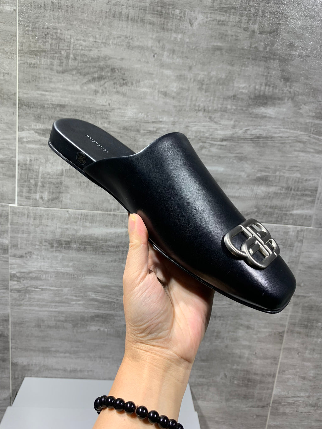Black slide sandal with silver buckle detail, held up by a hand