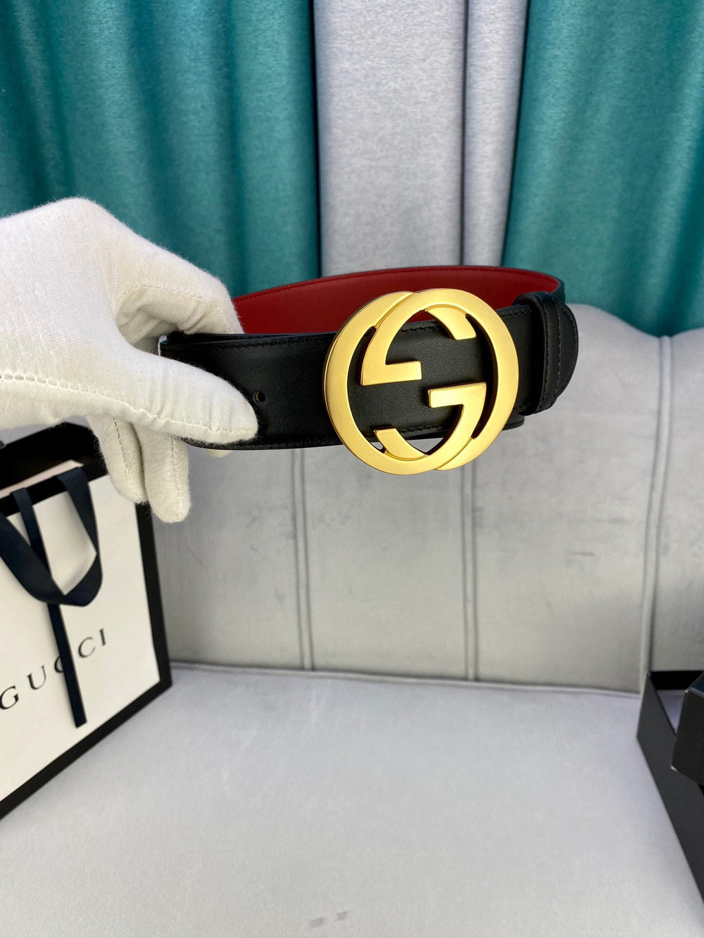 Black leather belt held by hand with gold-toned GG buckle and red interior