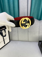 Black leather belt held by hand with gold-toned GG buckle and red interior